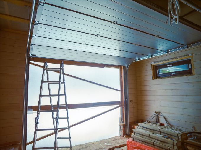 Interior of a garage under construction in Greer, SC, showing a silver sectional door in the open position with high-quality metal rollers and hinges installed along the overhead tracks.