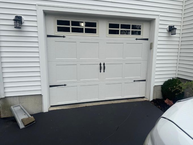 Exterior of a white carriage-style garage door with black hardware and windows on a home in Greer, SC, representing a system where mismatched parts or daily wear can lead to squeaking and grinding noises.