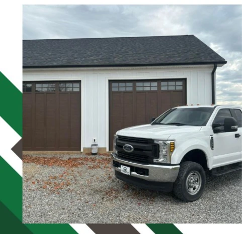 Two dark wood-grain carriage house garage doors with top-section windows installed on a white board-and-batten garage by Greer Garage Doors.