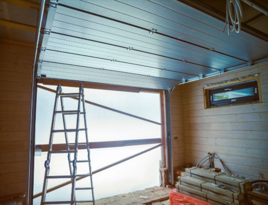 Professional installation of a silver metallic sectional garage door in a new residential construction project by Greer Garage Doors.