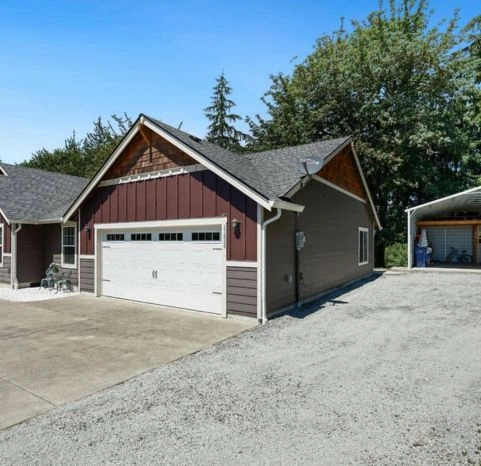 Residential garage door replacement featuring a white recessed-panel door with decorative handles and window inserts on a detached garage.