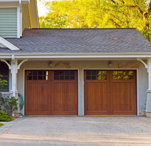 Two warm oak wood-grain carriage house garage doors with vertical planking and 6-lite window panes on a Craftsman-style home by Greer Garage Doors.