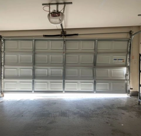Professional residential garage door track and hardware installation featuring a ceiling-mounted chain-drive opener and reinforced steel panels.