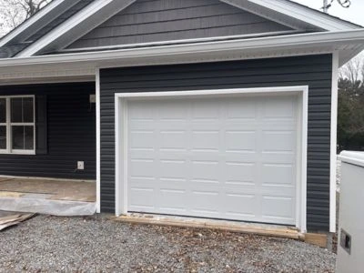 Classic white raised-panel garage door installed on a home with dark charcoal gray siding and white trim by Greer Garage Doors.
