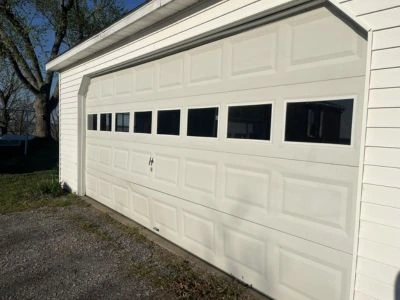 White double-car garage door featuring a row of rectangular windows for natural light, installed on a white-sided garage by Greer Garage Doors.